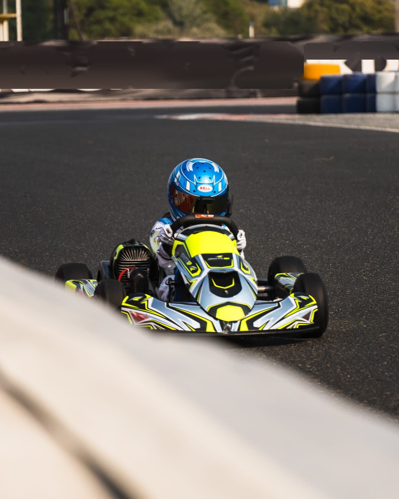 Bambino kart head-on past the pit wall, circuit banners behind